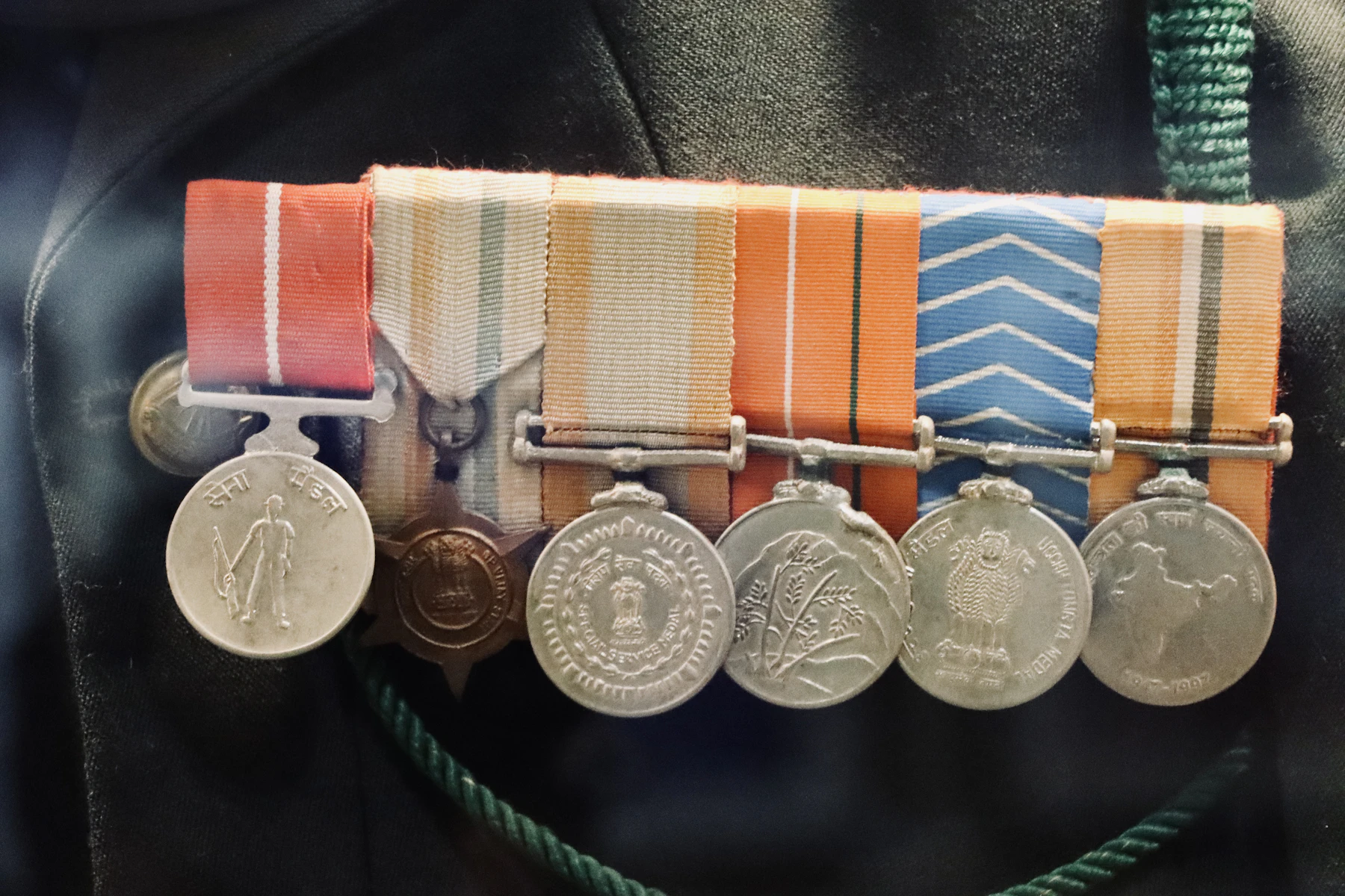 A bar of six silver medals on orange, white and blue ribbons pinned to a dark uniform