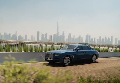 A blue car driving down a road in front of a city