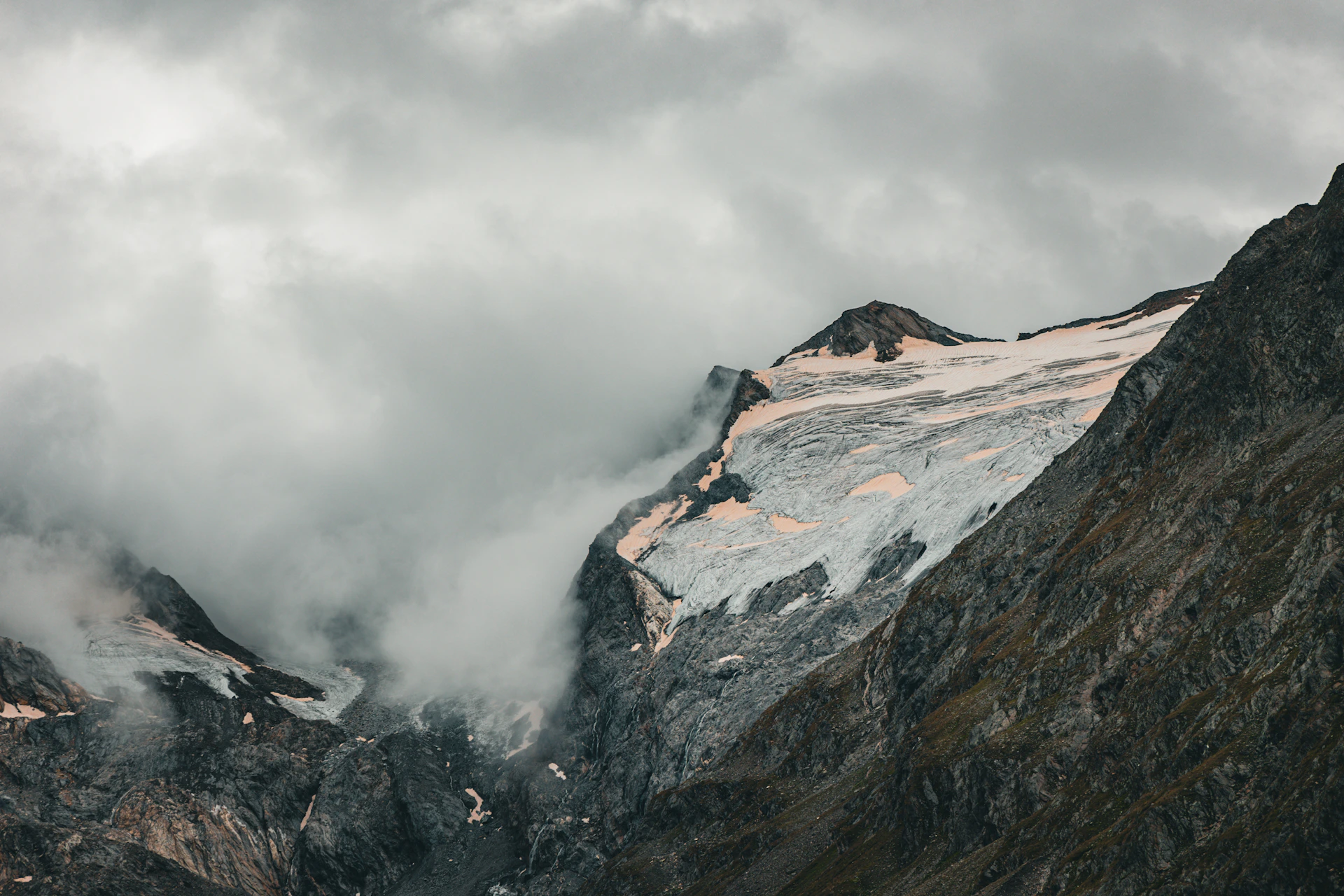 A mountain covered in snow and clouds under a cloudy sky