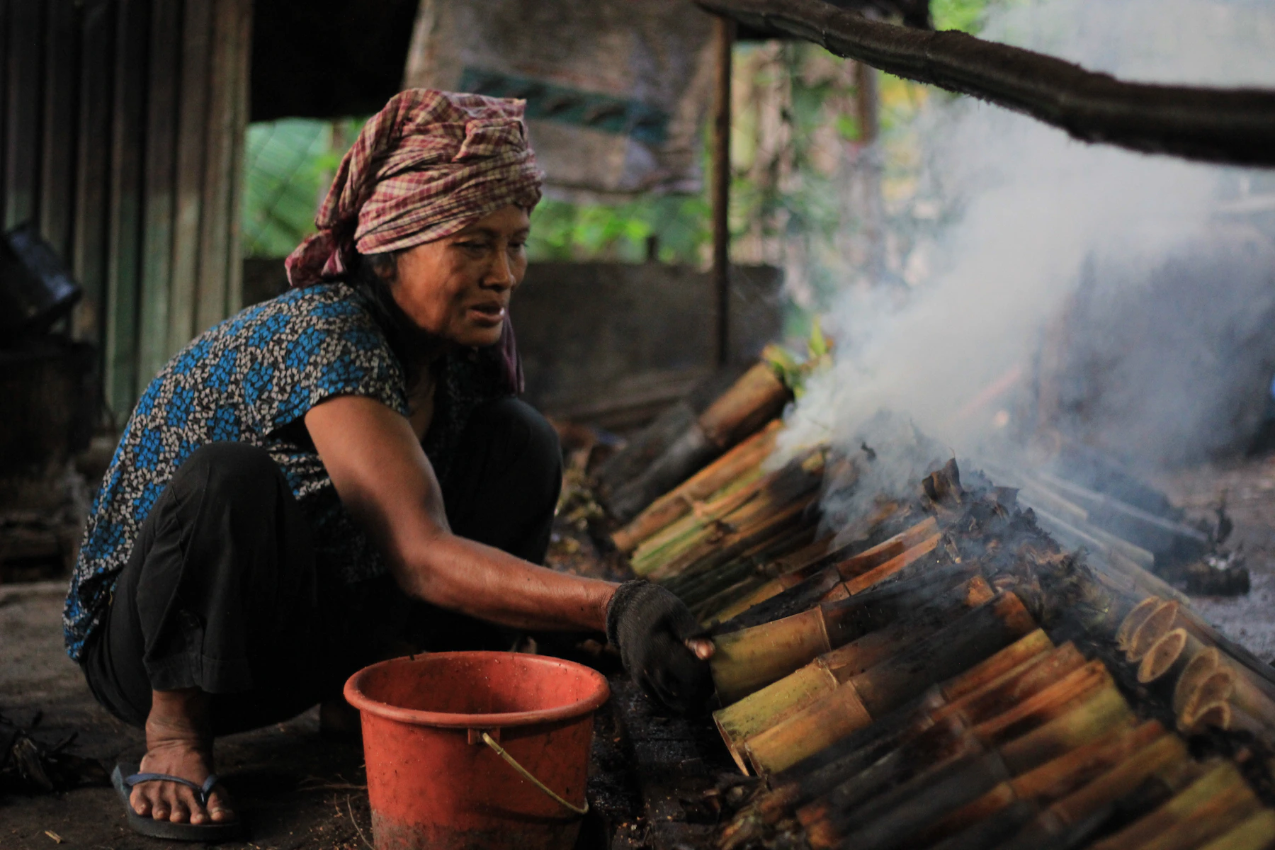 Cambodian woman tending bamboo tubes of traditional kralan sticky rice over a wood fire