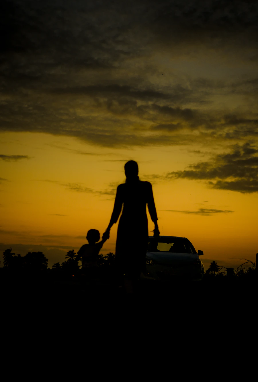 An adult holding a child's hand at sunset