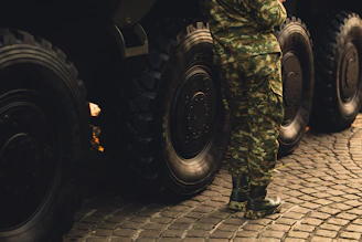 A man in camouflage standing next to a large truck