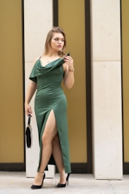 A woman in a green dress leaning against a wall