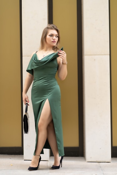 A woman in a green dress leaning against a wall