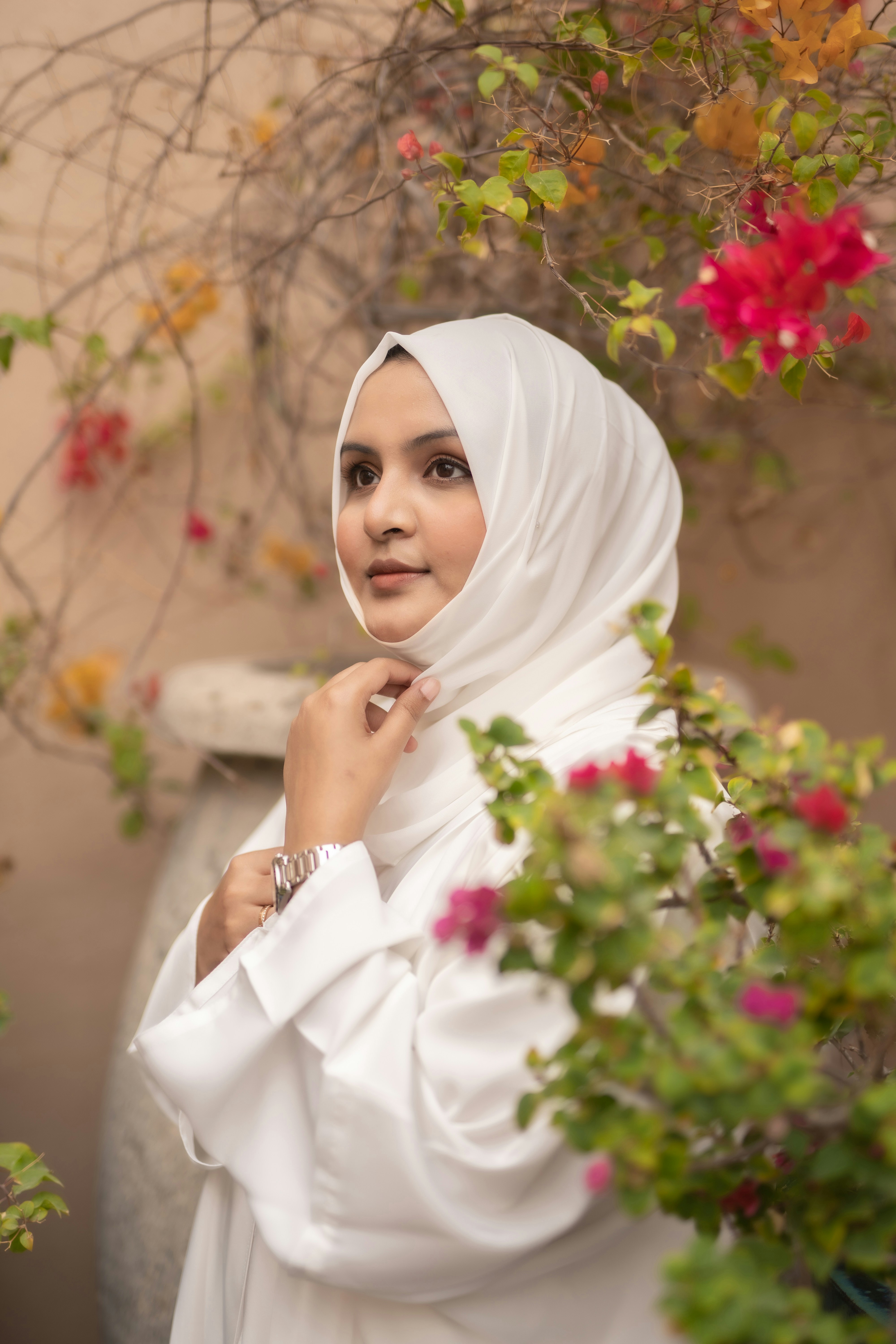 Seorang wanita mengenakan jilbab putih berdiri di depan semak-semak
