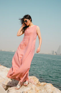 A woman in a pink dress standing on a rock by the water