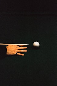 A person's hand reaching for a ball with a cue in it