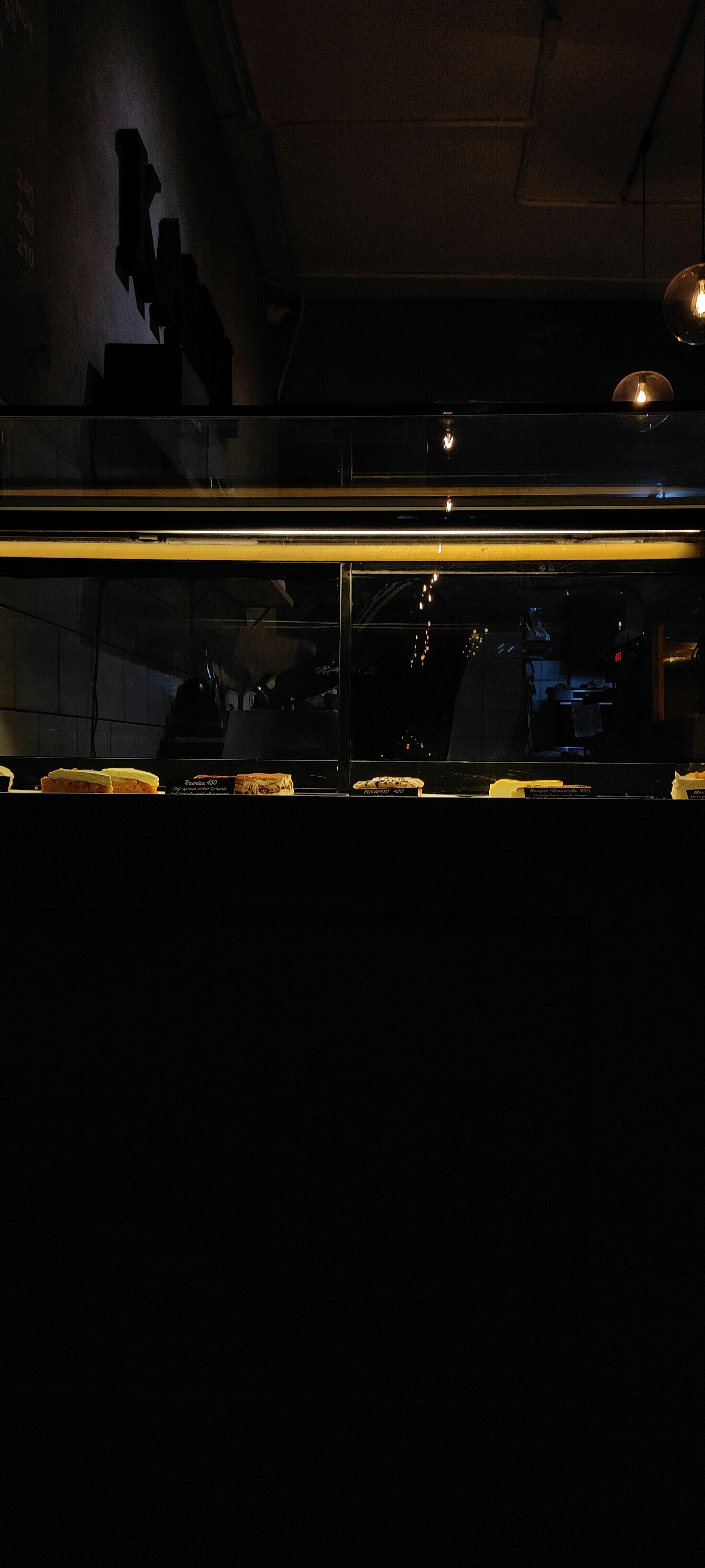 Interior bakery premium yang nyaman dengan pencahayaan emas hangat, display dessert, bayangan dalam, rak kayu gelap, pencahayaan atmosferik