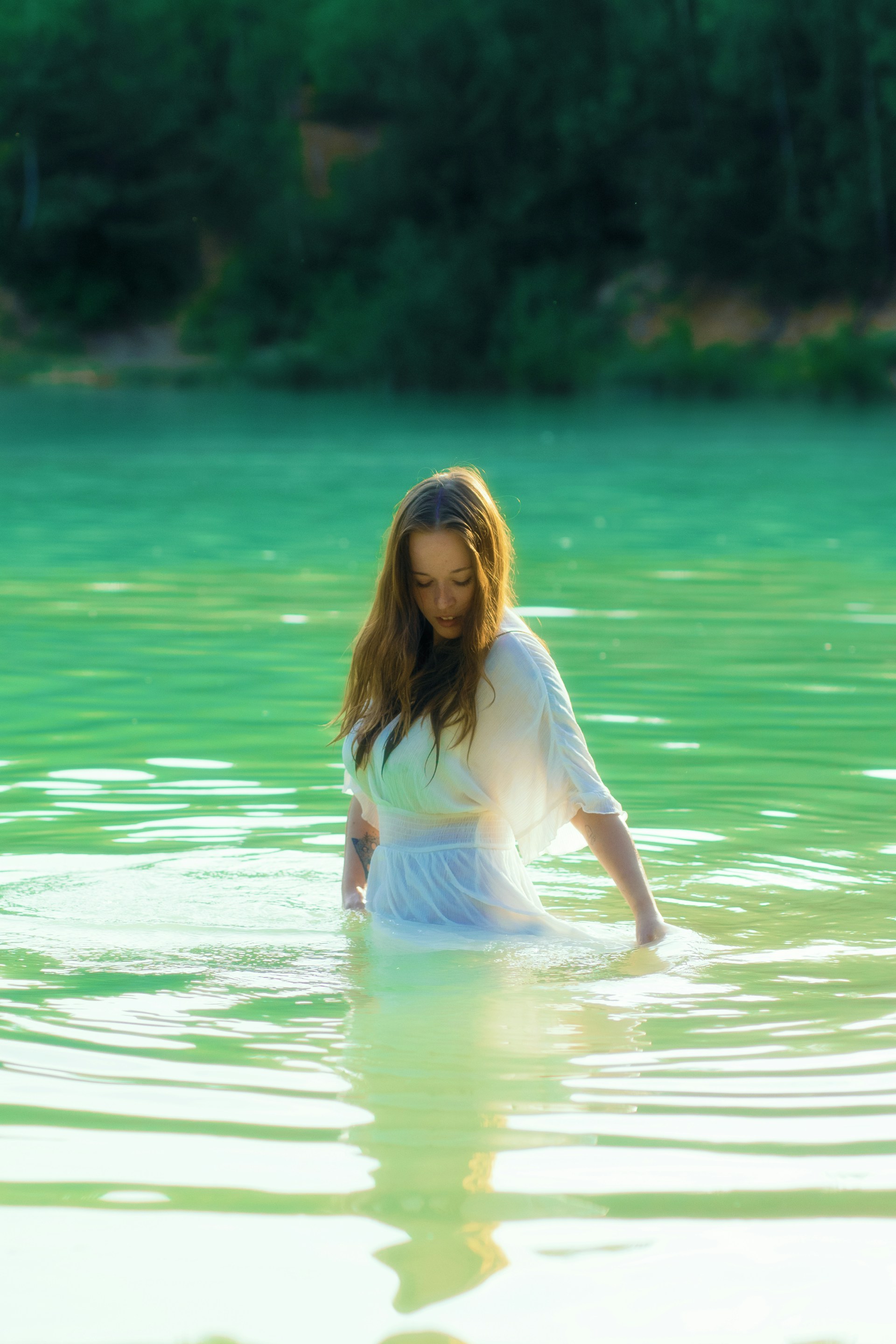 A woman in a white dress wading in a lake