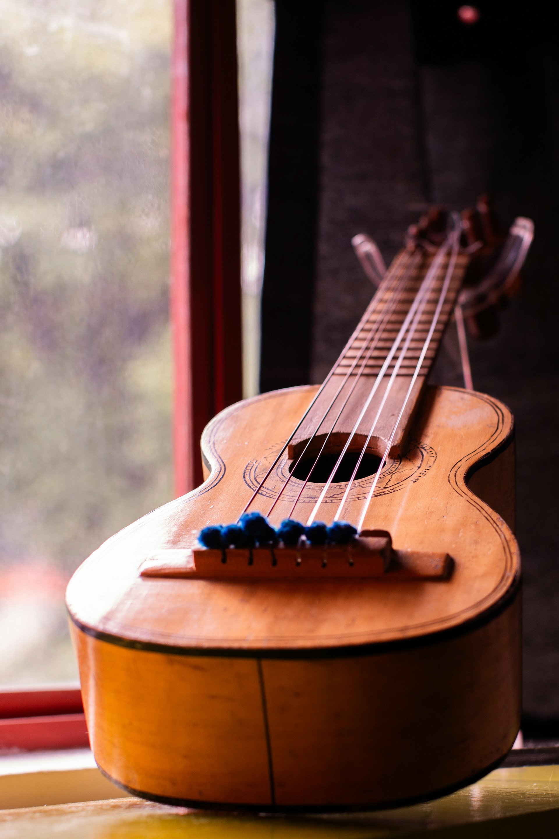 A ukulele sitting on a window sill in front of a window