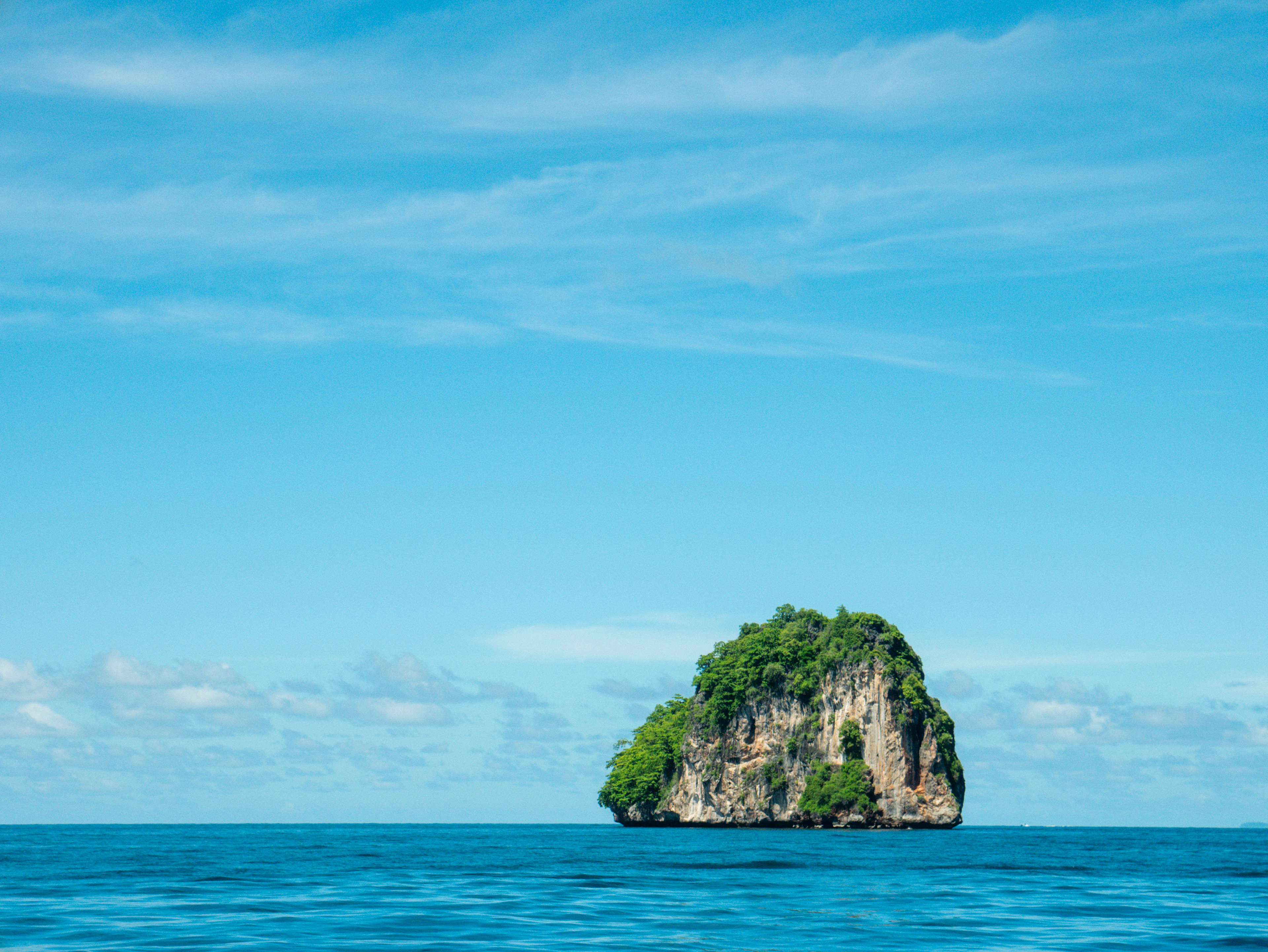 A solitary jungle-topped limestone island rock rises from calm deep-blue sea.