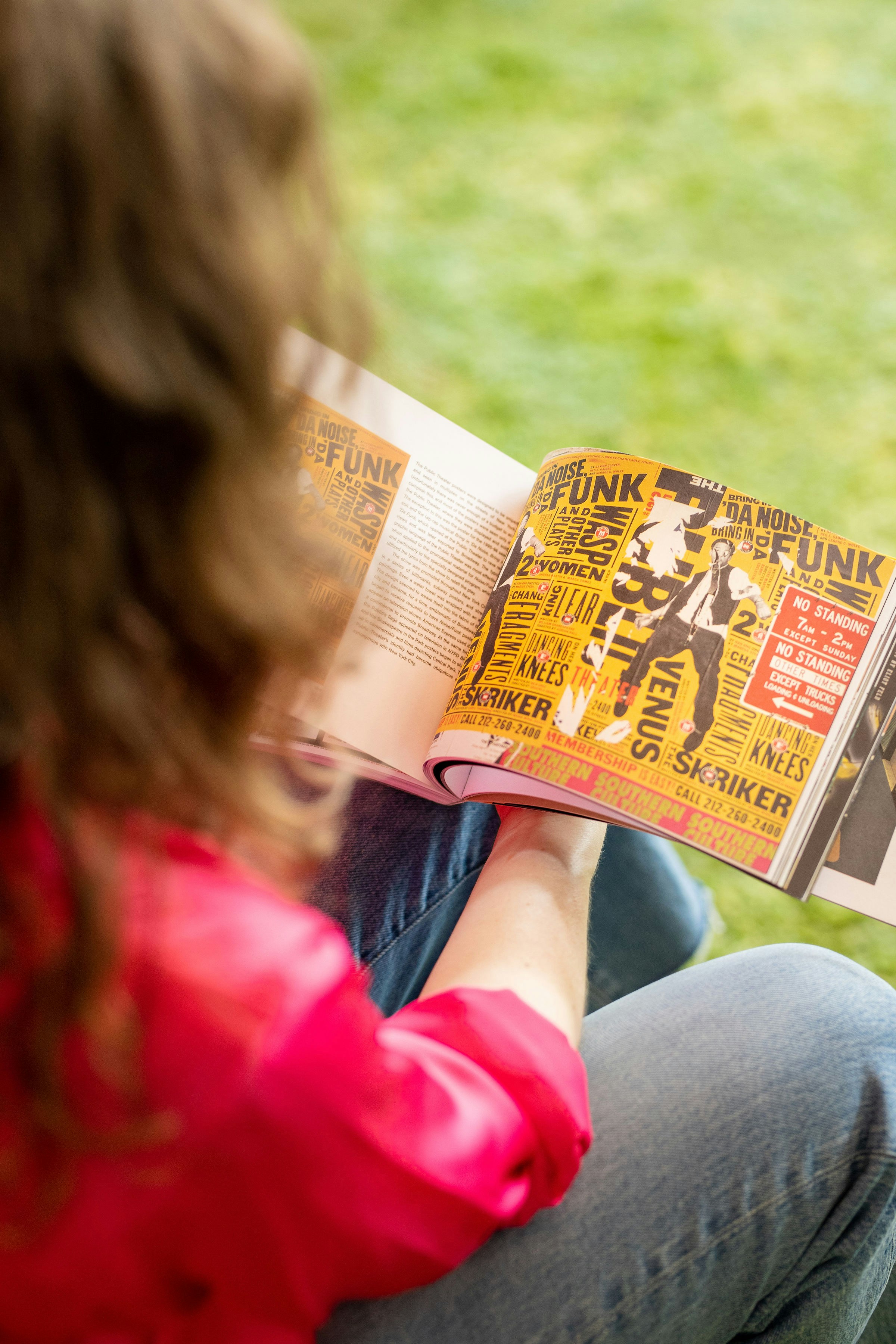 A woman reading a newspaper sitting on the grass