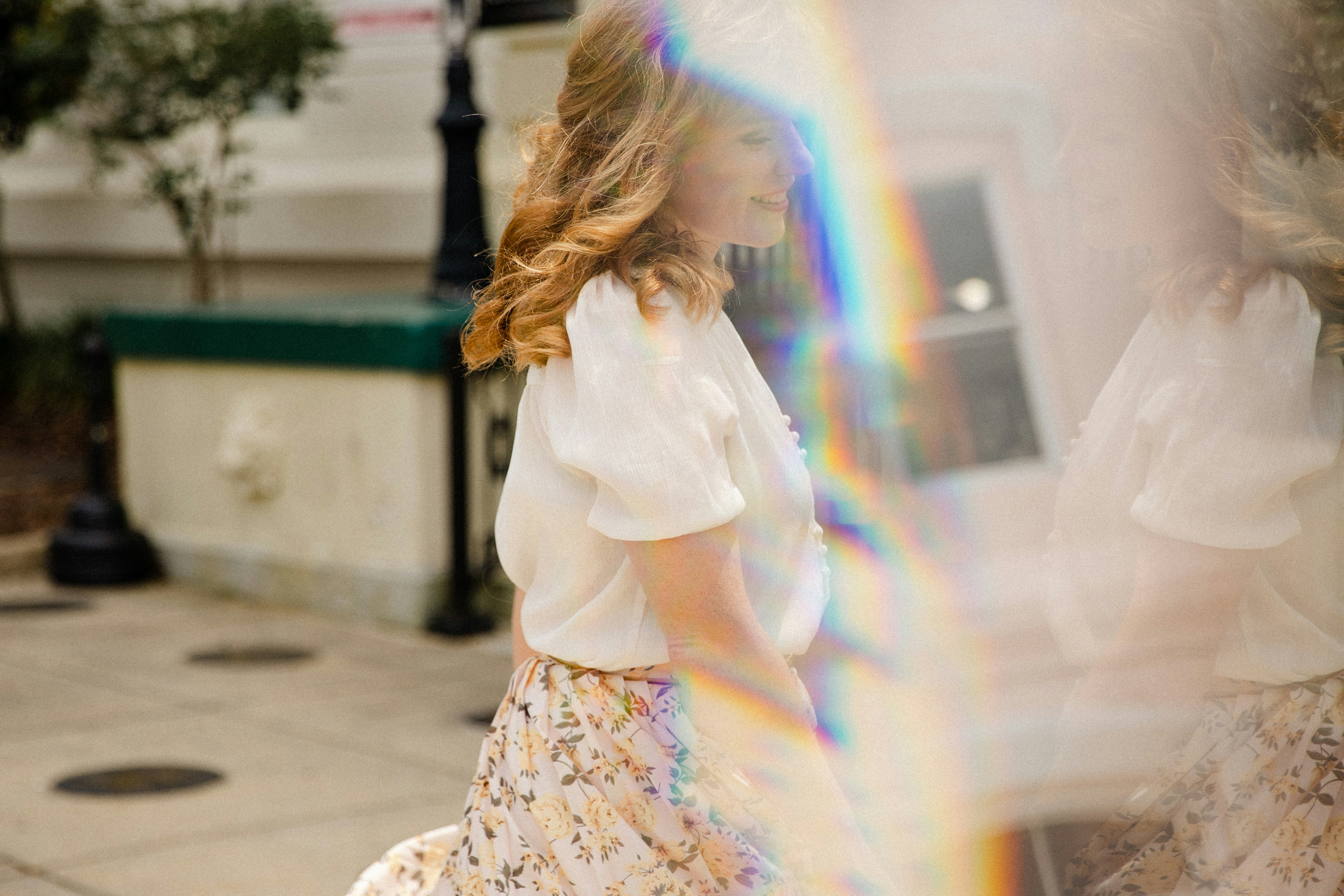 A woman walking down a sidewalk with a rainbow in the background