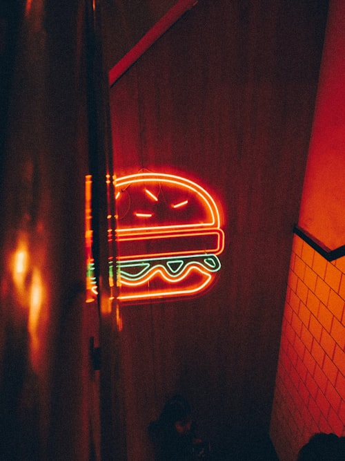 A red and green neon hamburger sign glowing on a dark wall