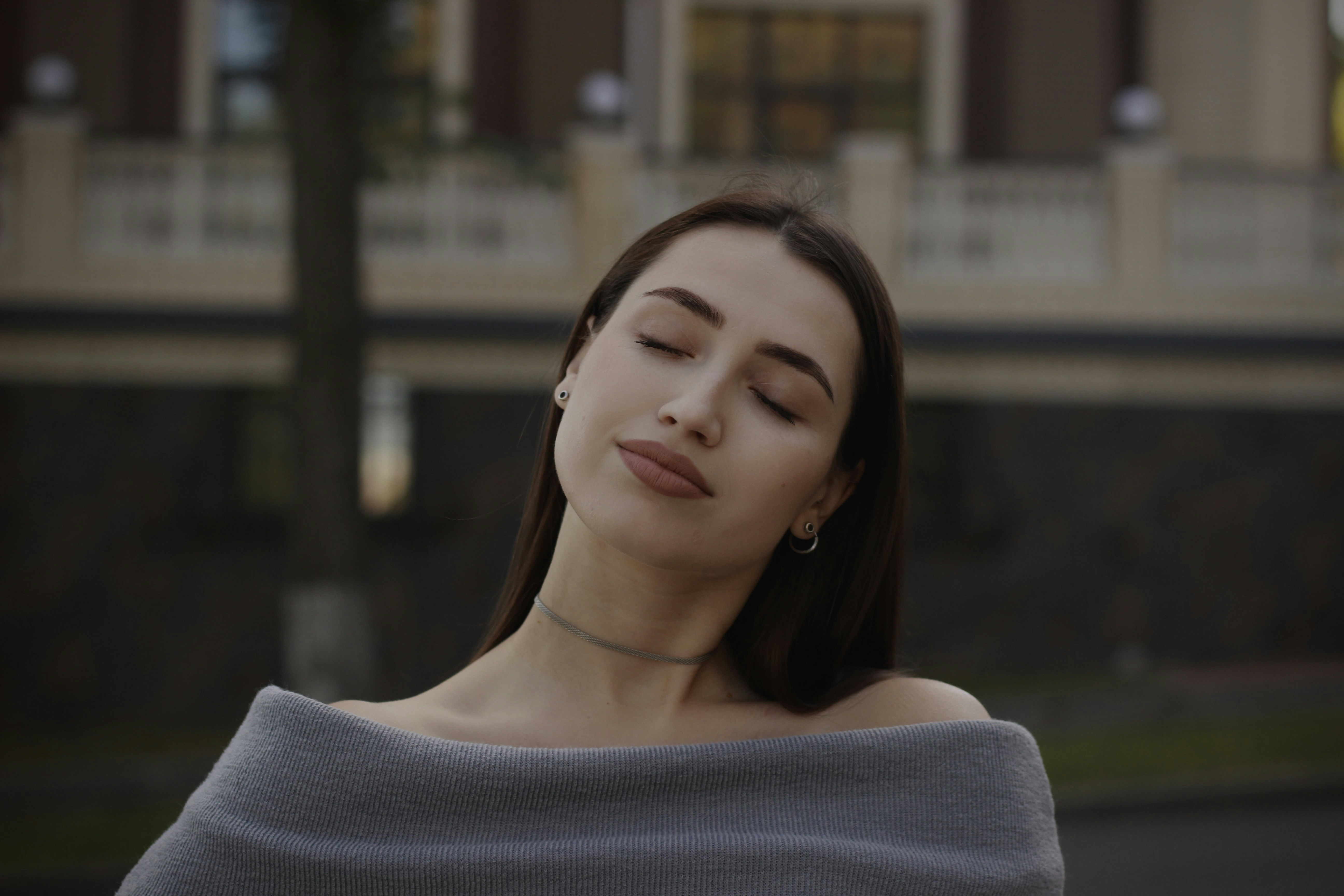 A woman with her eyes closed standing in front of a building