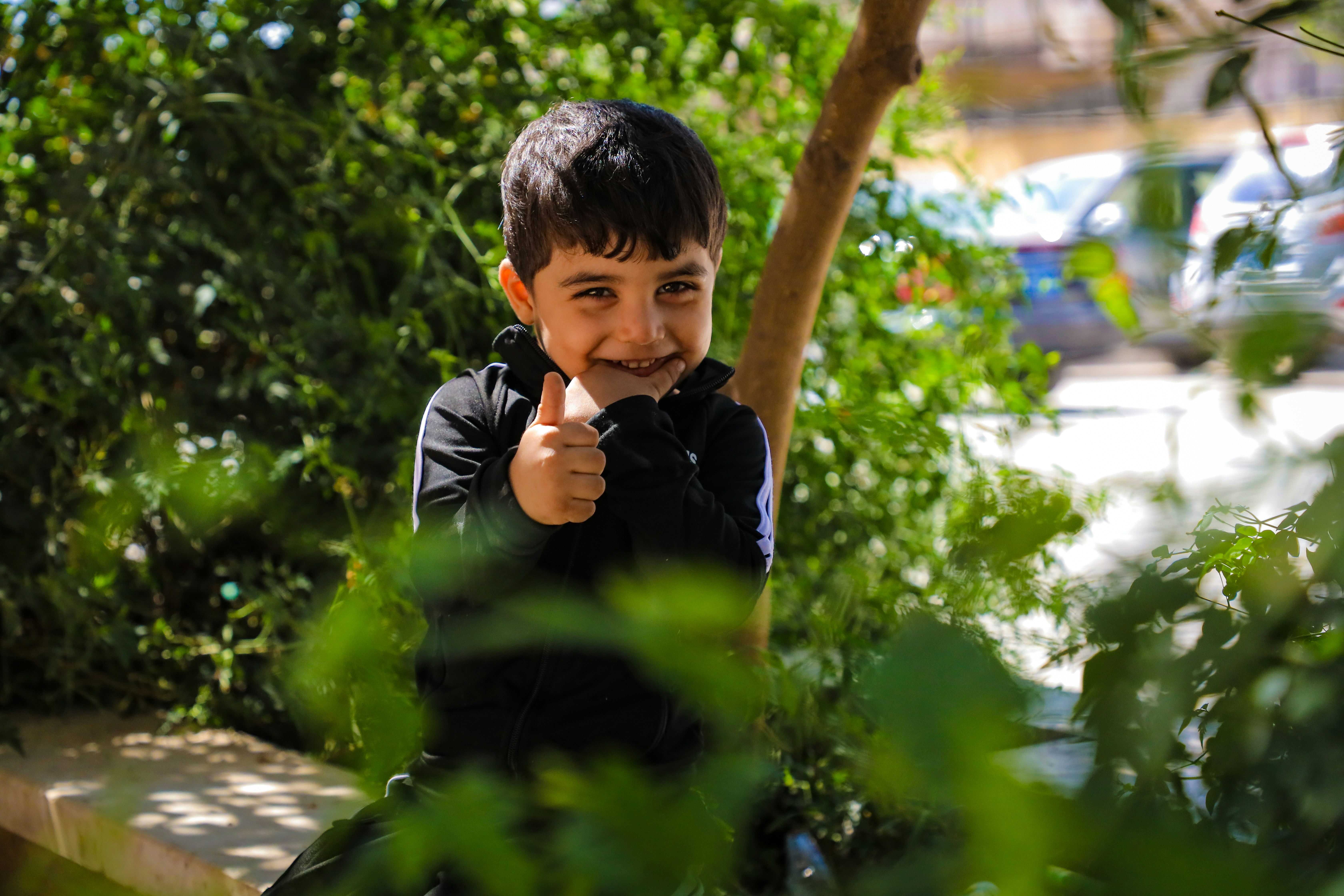 A young boy sitting on a bench with a finger in his mouth