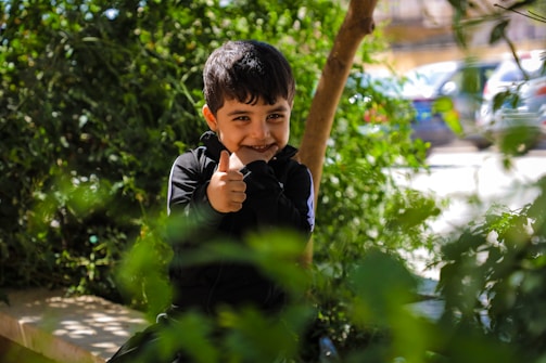 A young boy sitting on a bench with a finger in his mouth