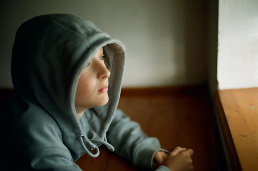 A young child sitting on a wooden floor next to a window
