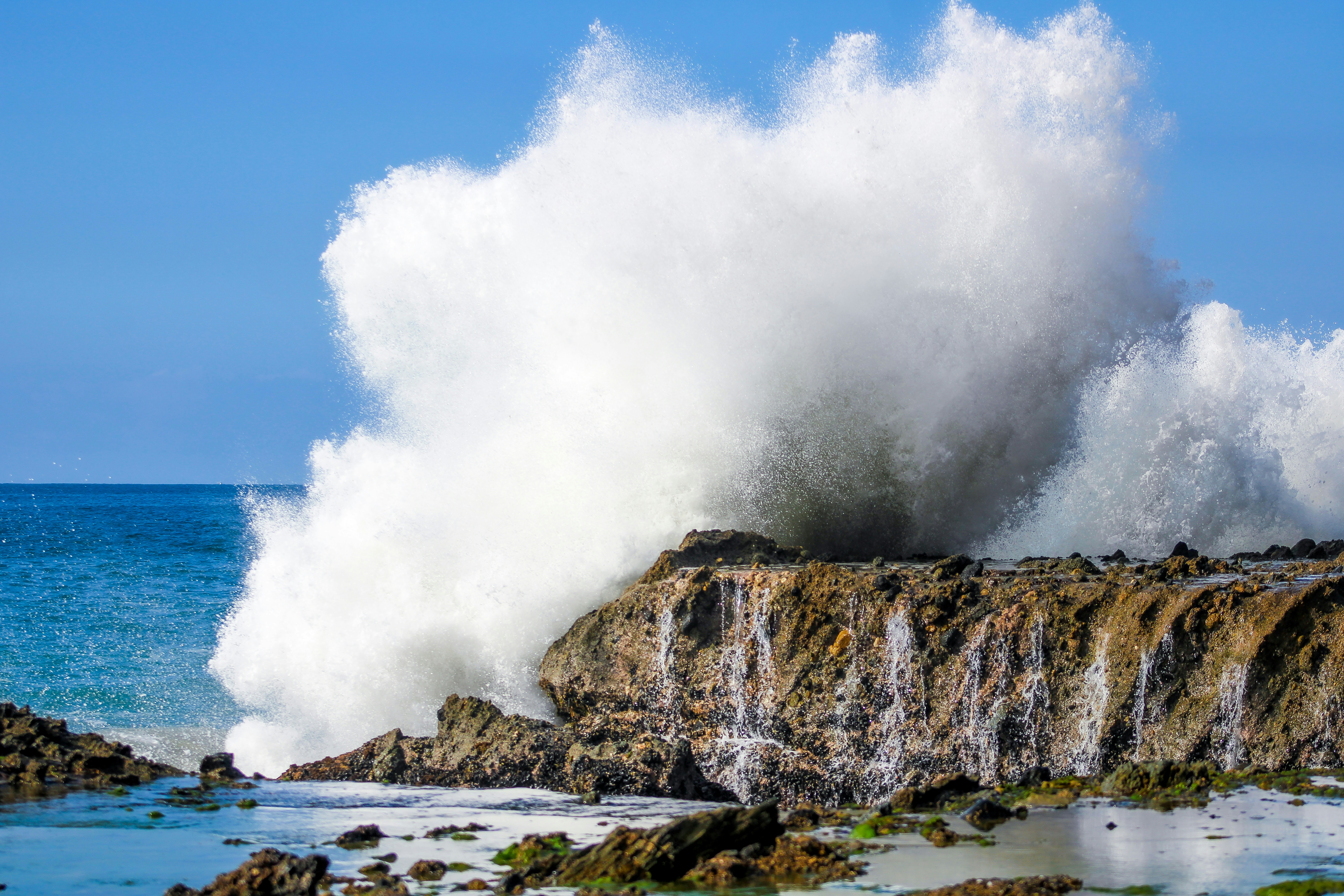 A large wave crashes into the rocks near the ocean