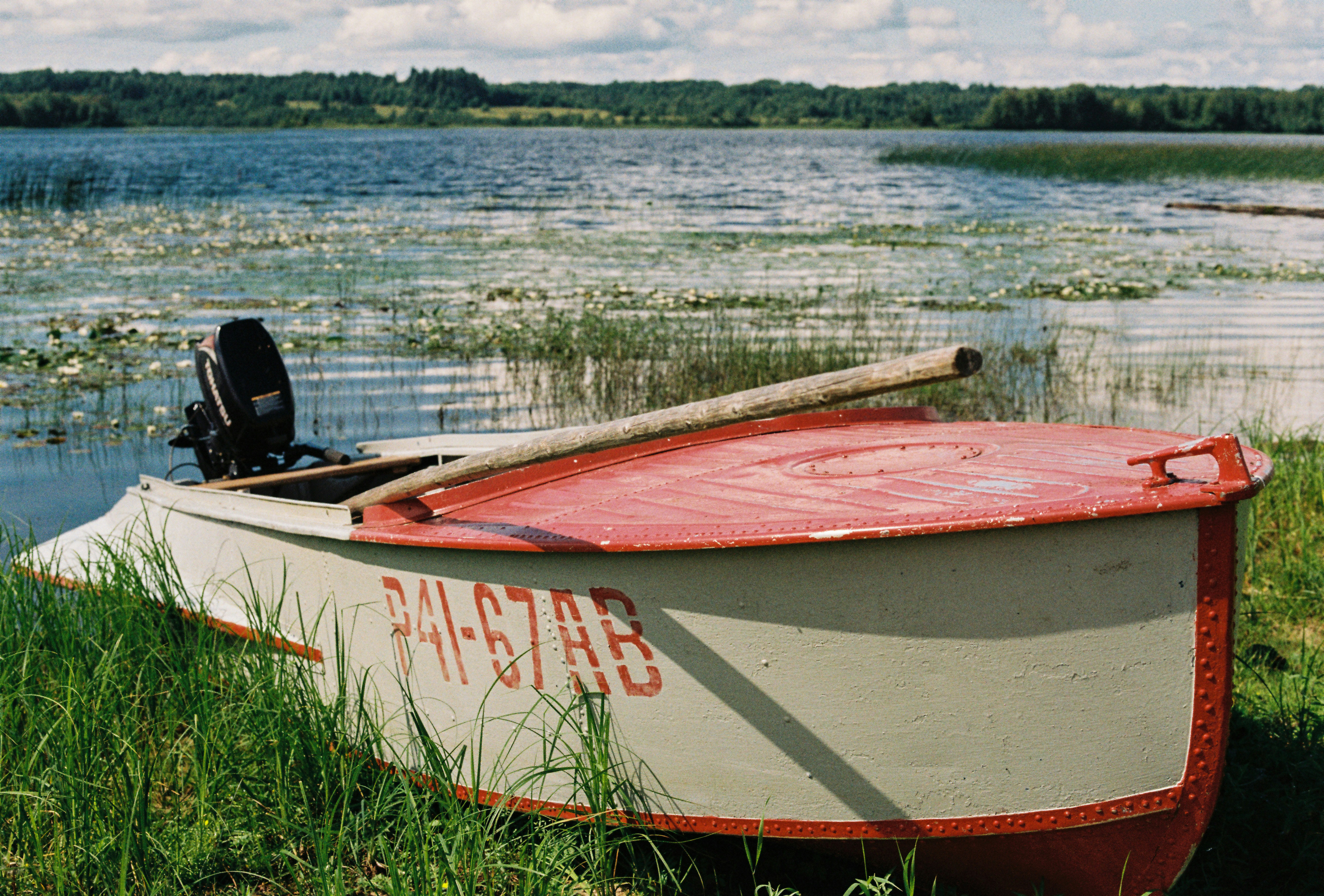 A red and white boat sitting on top of a grass covered field