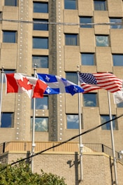 Three american and canadian flags flying in front of a building