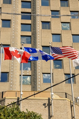 Three american and canadian flags flying in front of a building