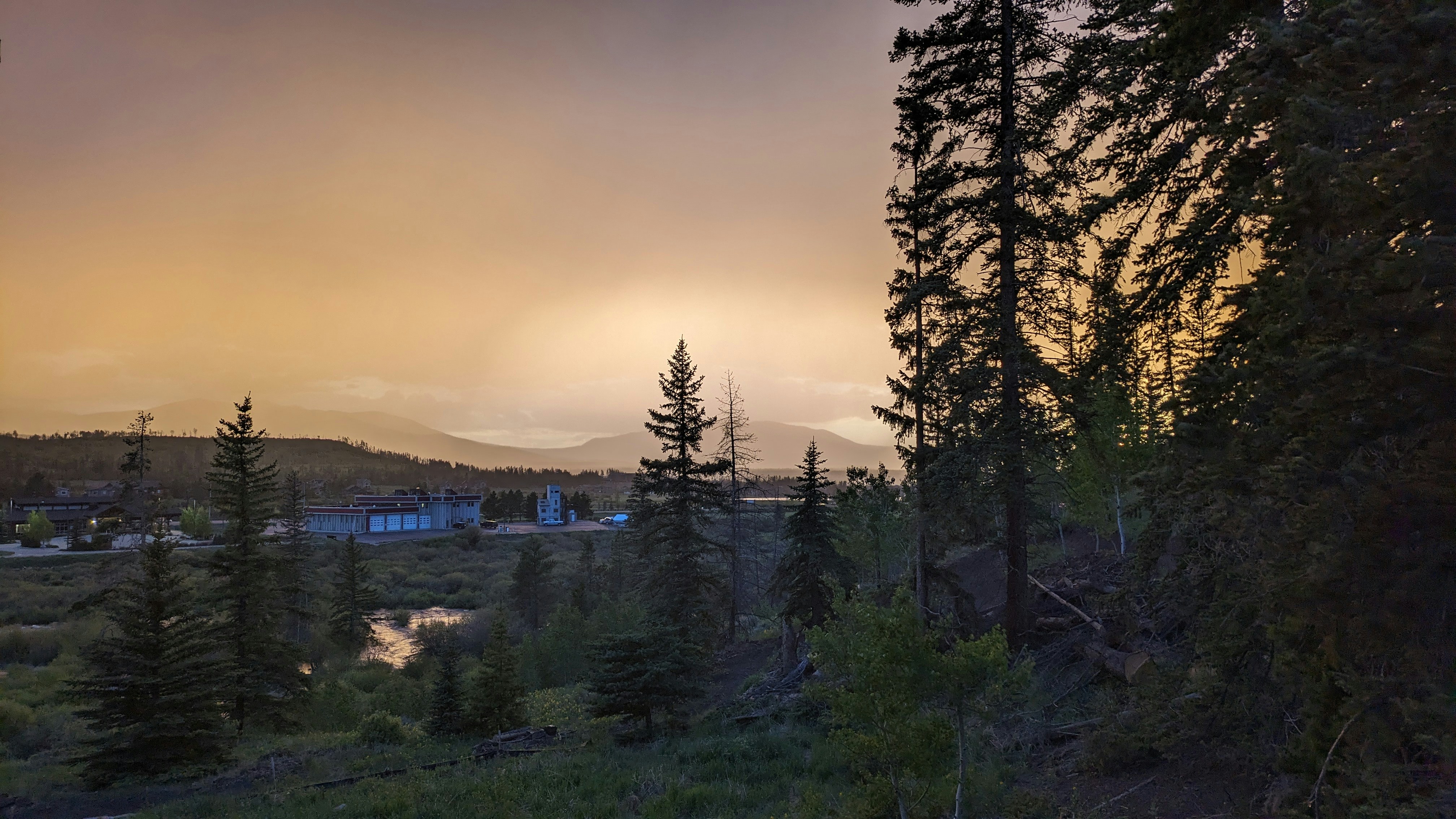 Golden sunset over Bir valley with silhouette of pine trees and distant snow peaks glowing orange