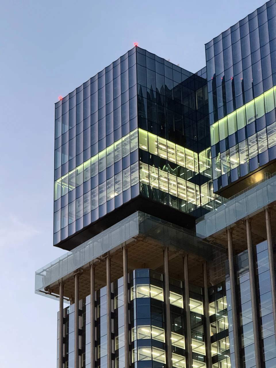 Modern glass and steel skyscraper with two-level windows reflecting cityscape at night under green lighting