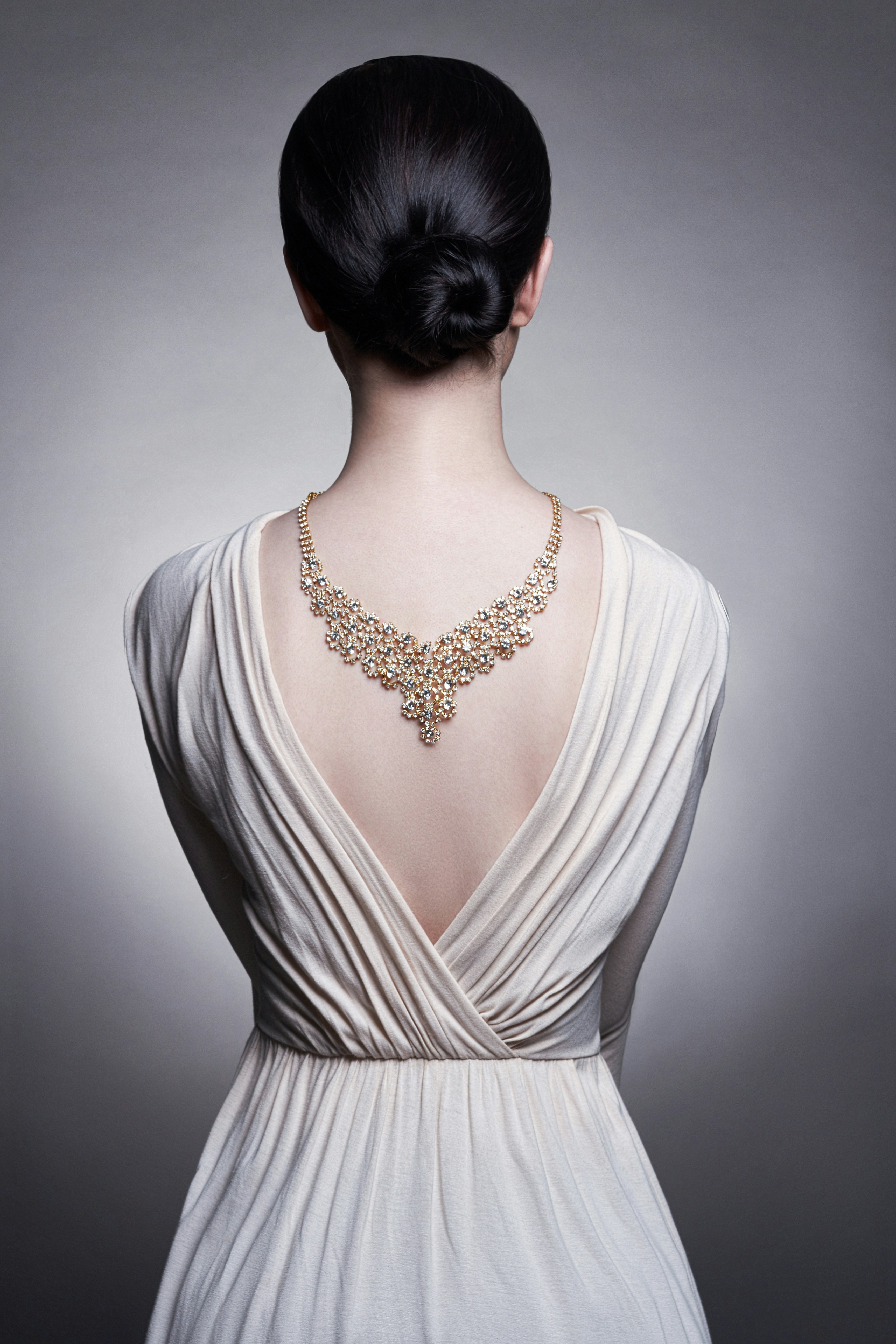 Woman modeling a sparkling gold necklace on her upper back.