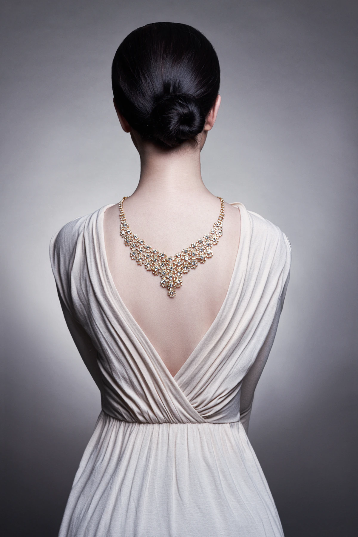 Adult woman in a white draped gown seen from behind wearing a statement diamond back necklace