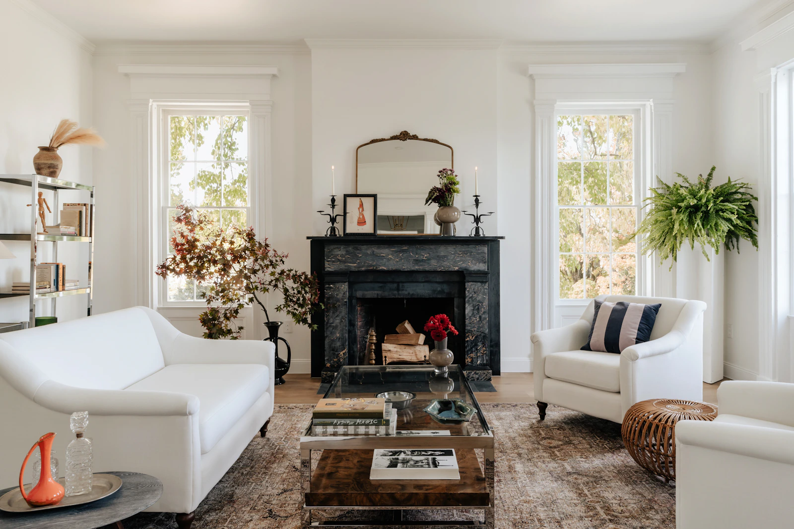 Sunlit living room with white sofas, leafy plants, and a marble fireplace
