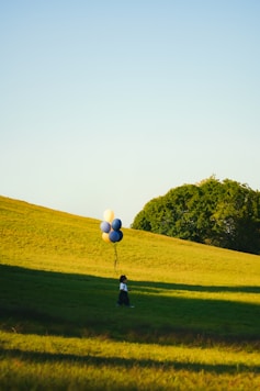 A person standing in a field with a bunch of balloons
