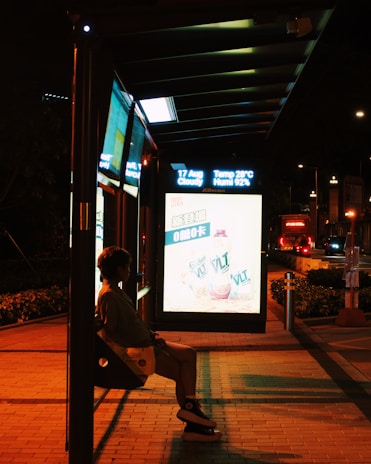 A person sitting on a bench in front of a bus stop