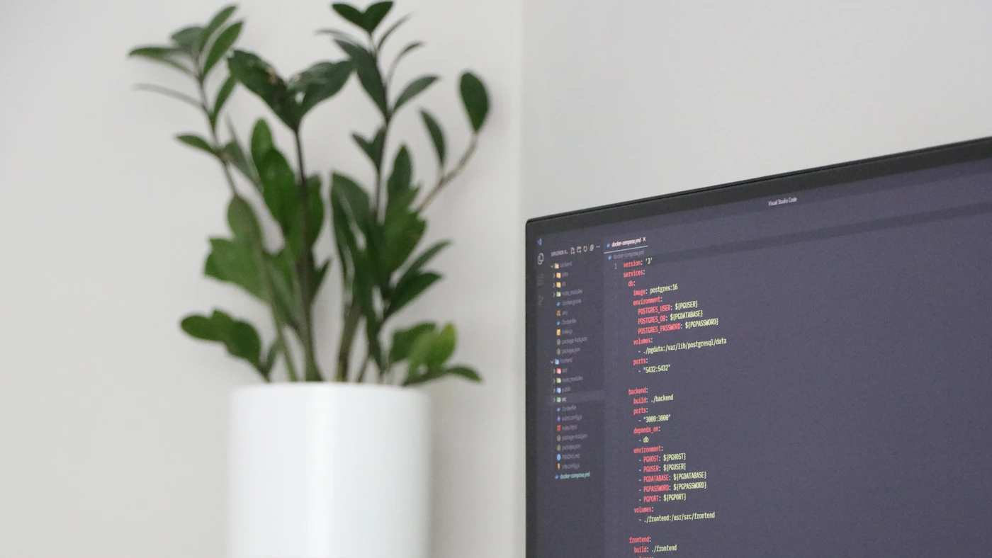 A monitor showing code beside a green plant