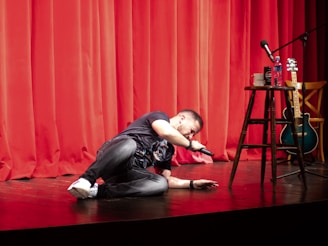 A man kneeling on the floor in front of a red curtain