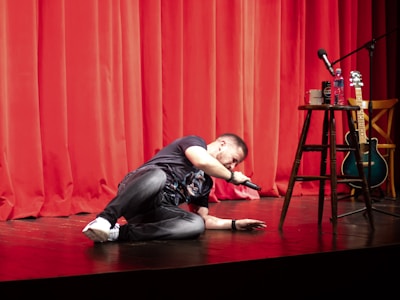 A man kneeling on the floor in front of a red curtain