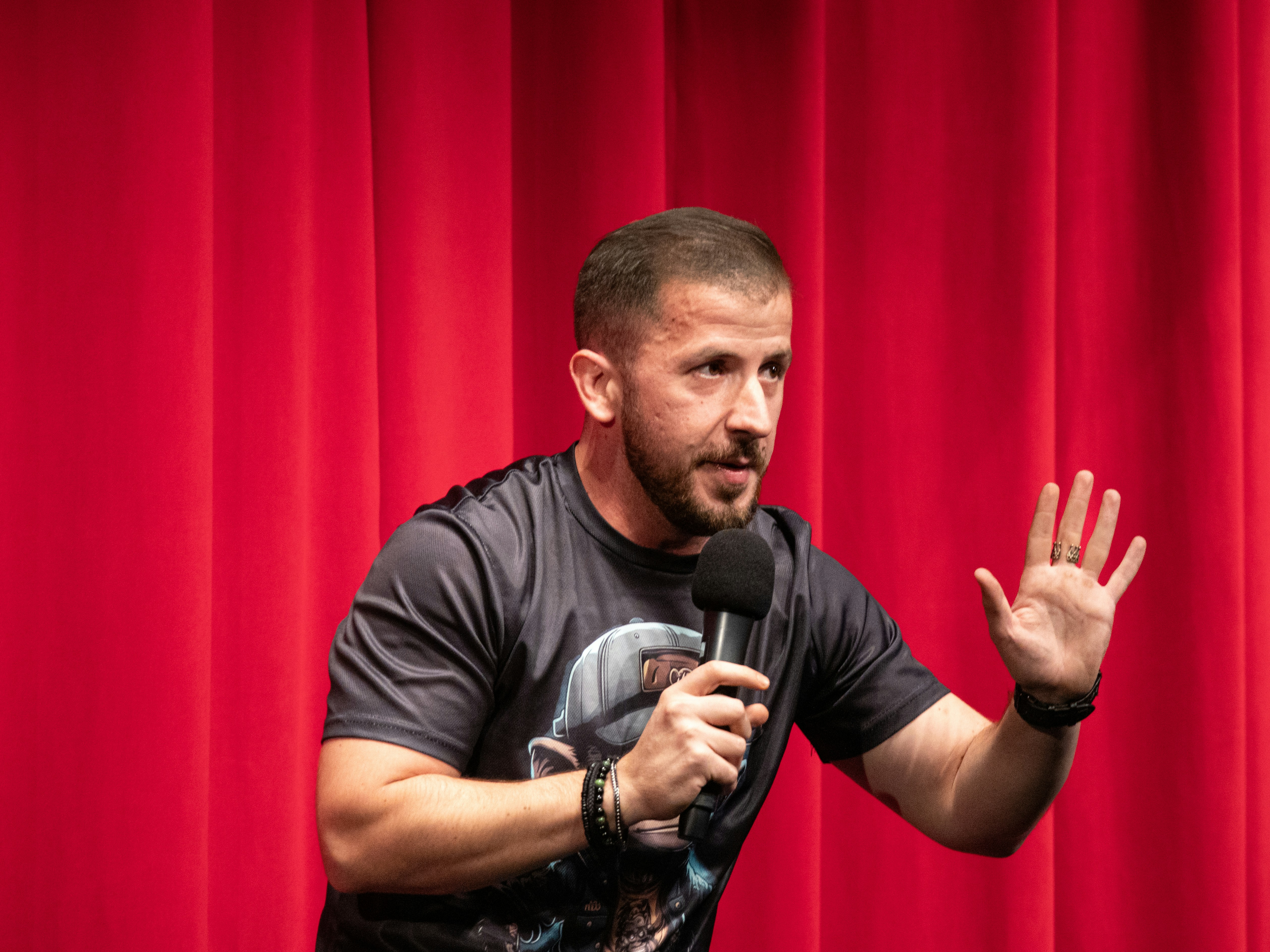 A man standing in front of a red curtain holding a microphone, 