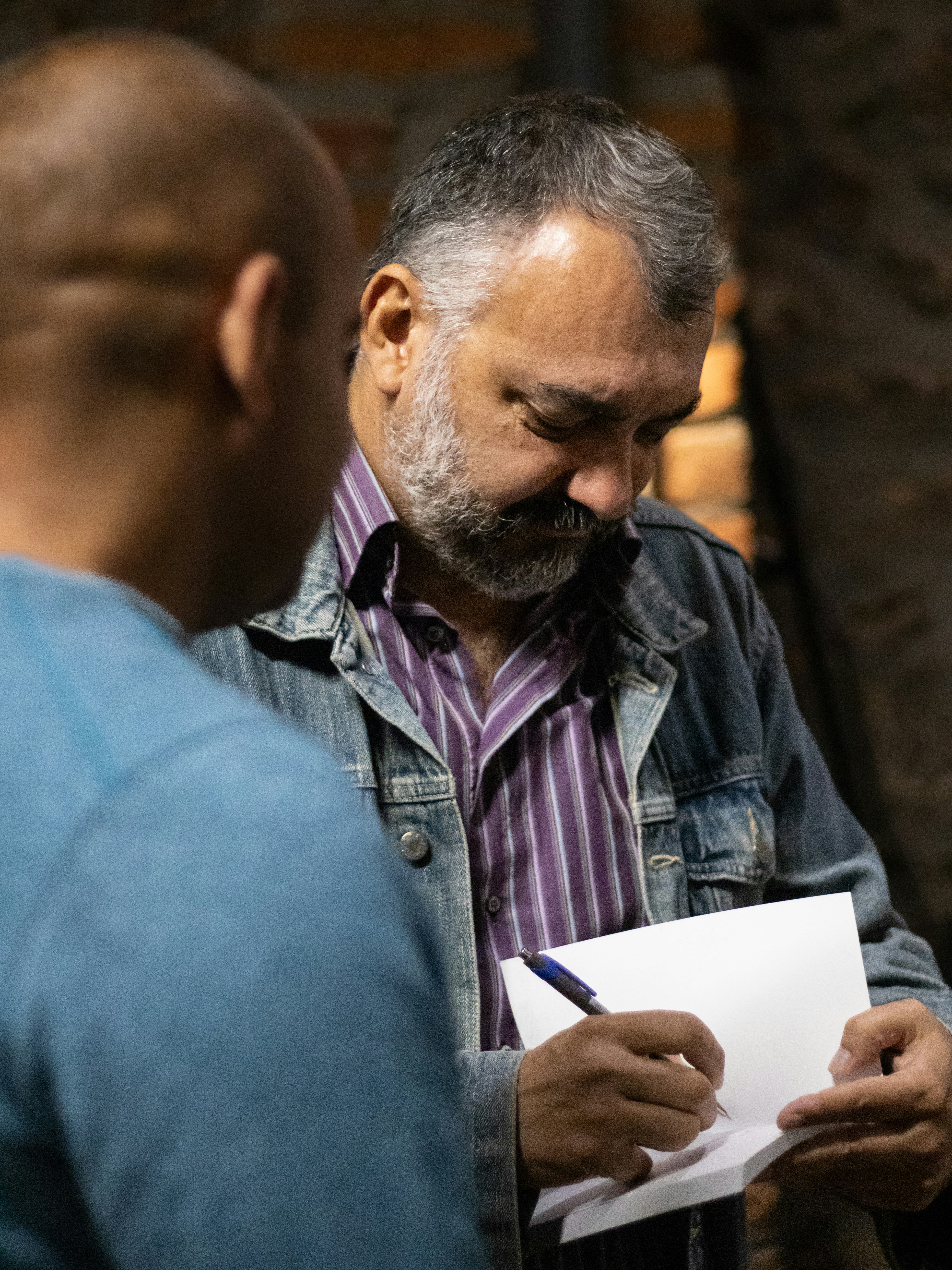 A man in a denim jacket writing on a piece of paper