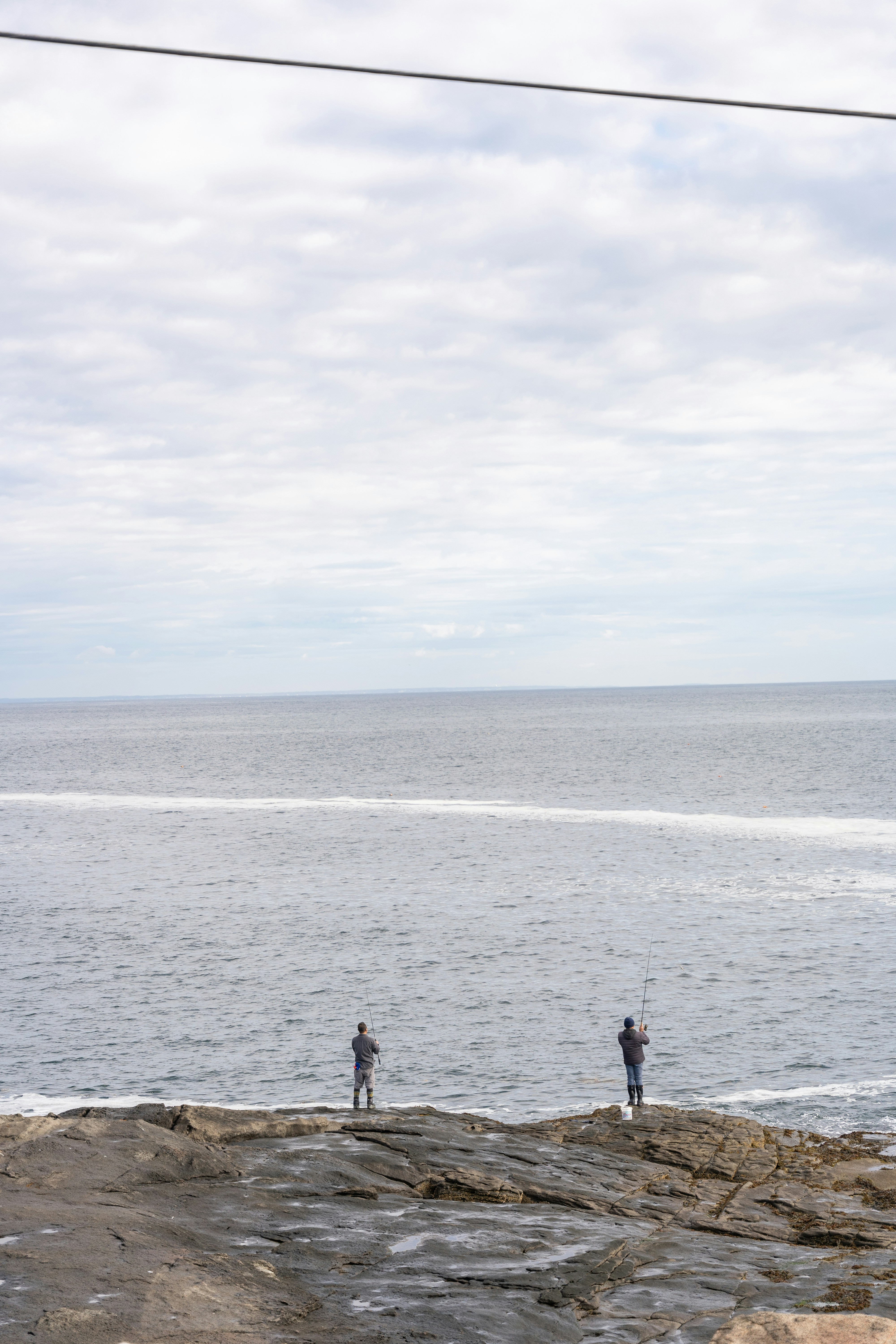 A couple of people standing on top of a cliff near the ocean