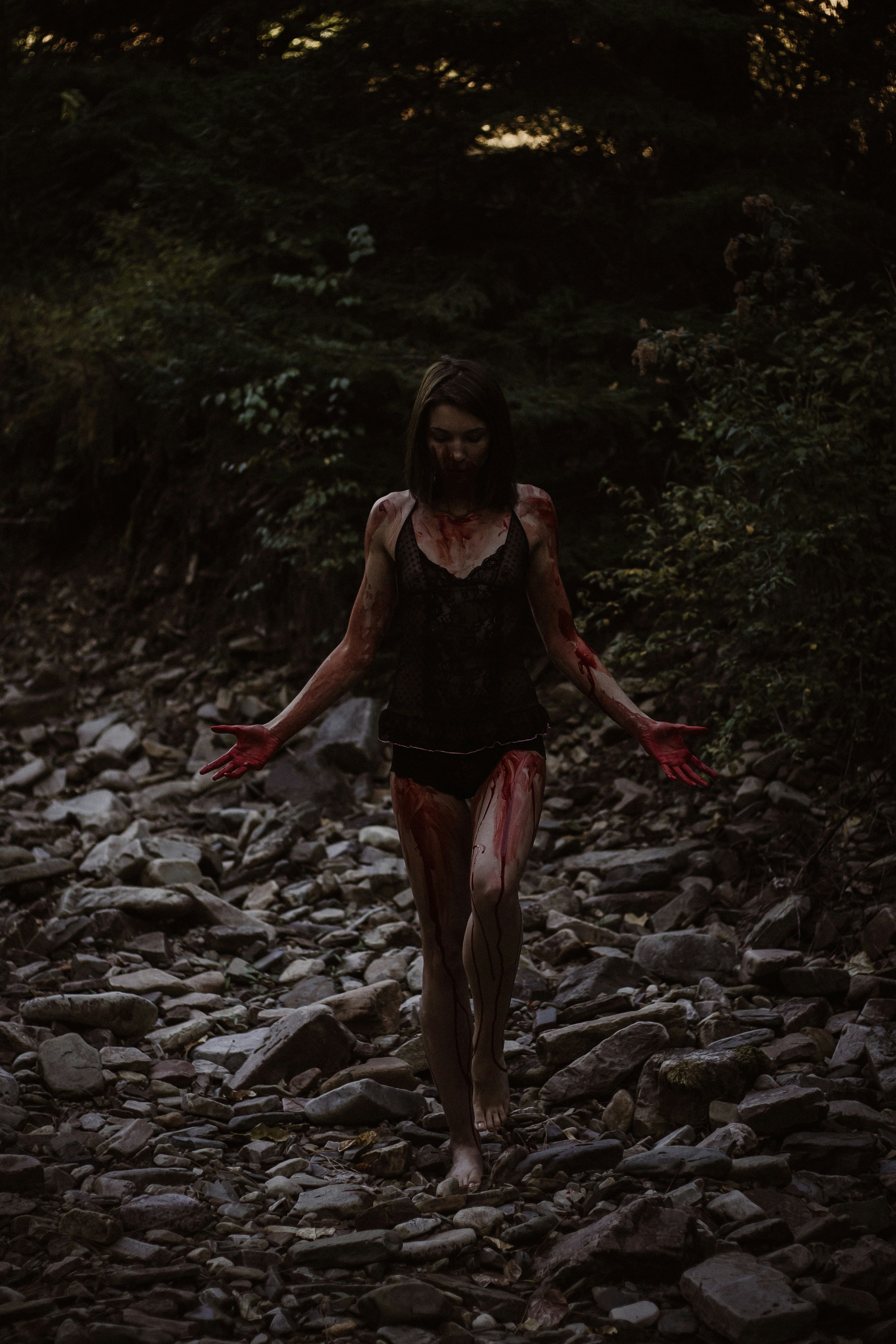 A woman with blood on her body walking on a rocky path