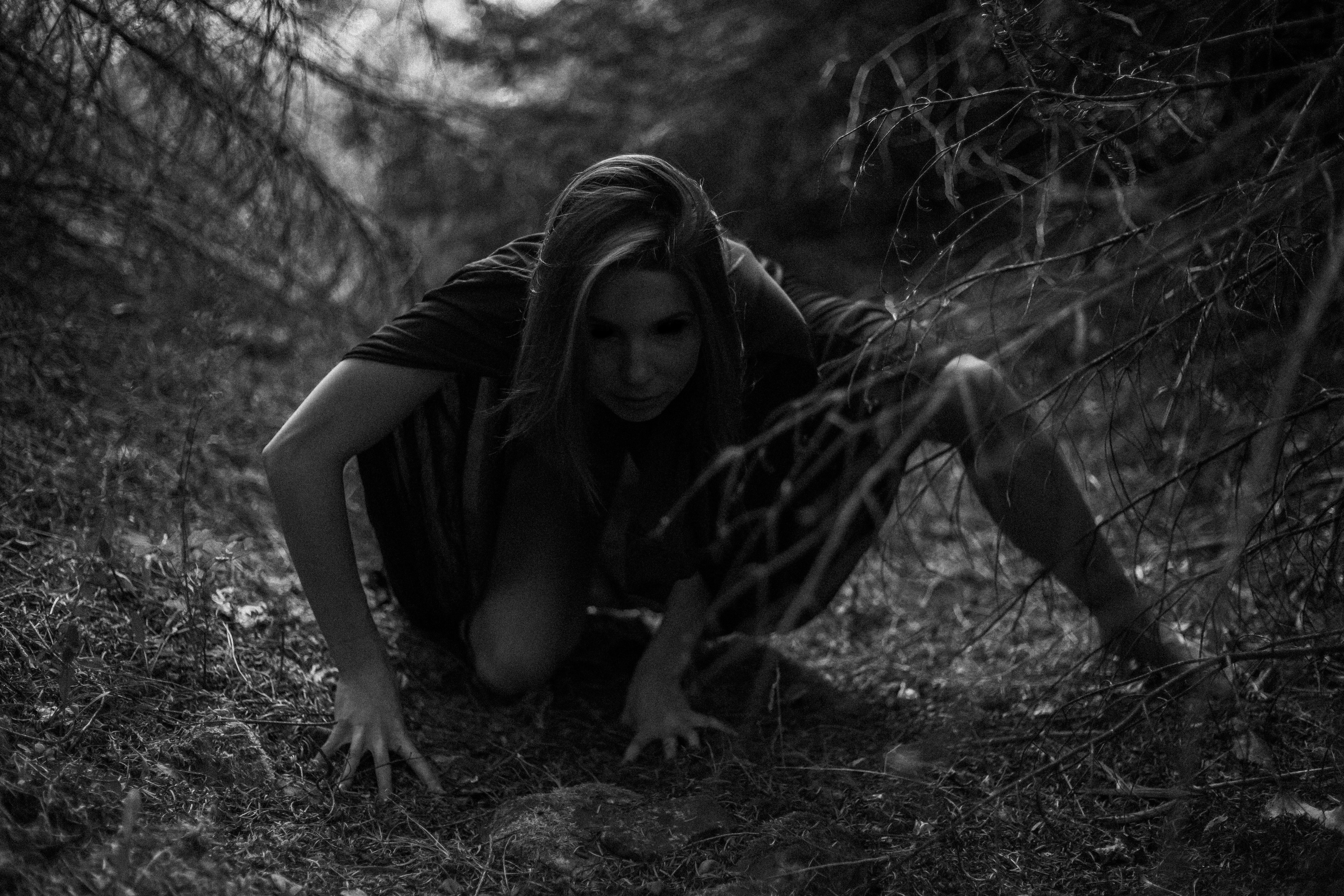 A man in a hoodie crouches down in the woods