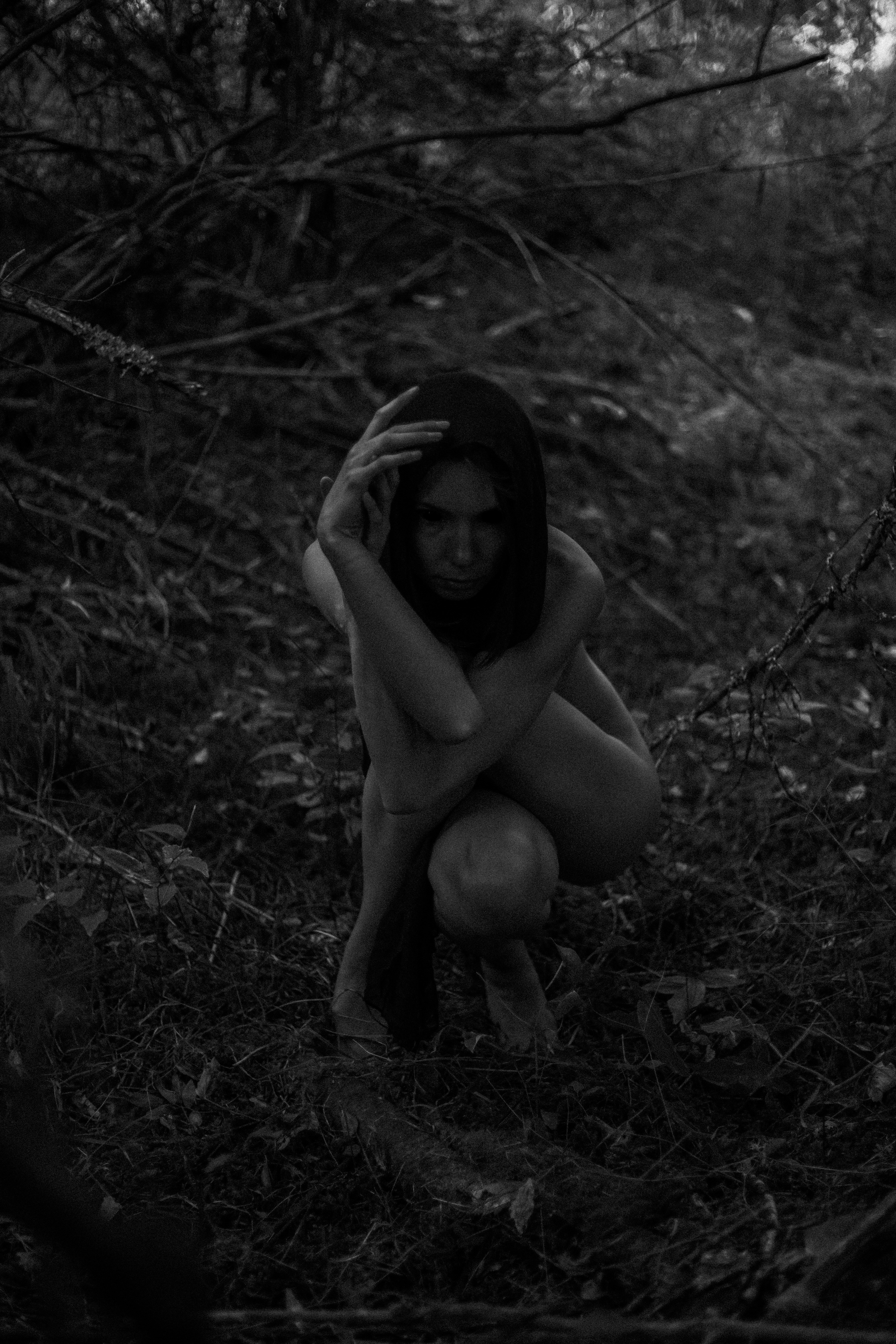 A naked woman crouches in the woods