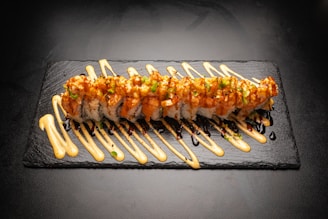 A black plate topped with sushi covered in sauce