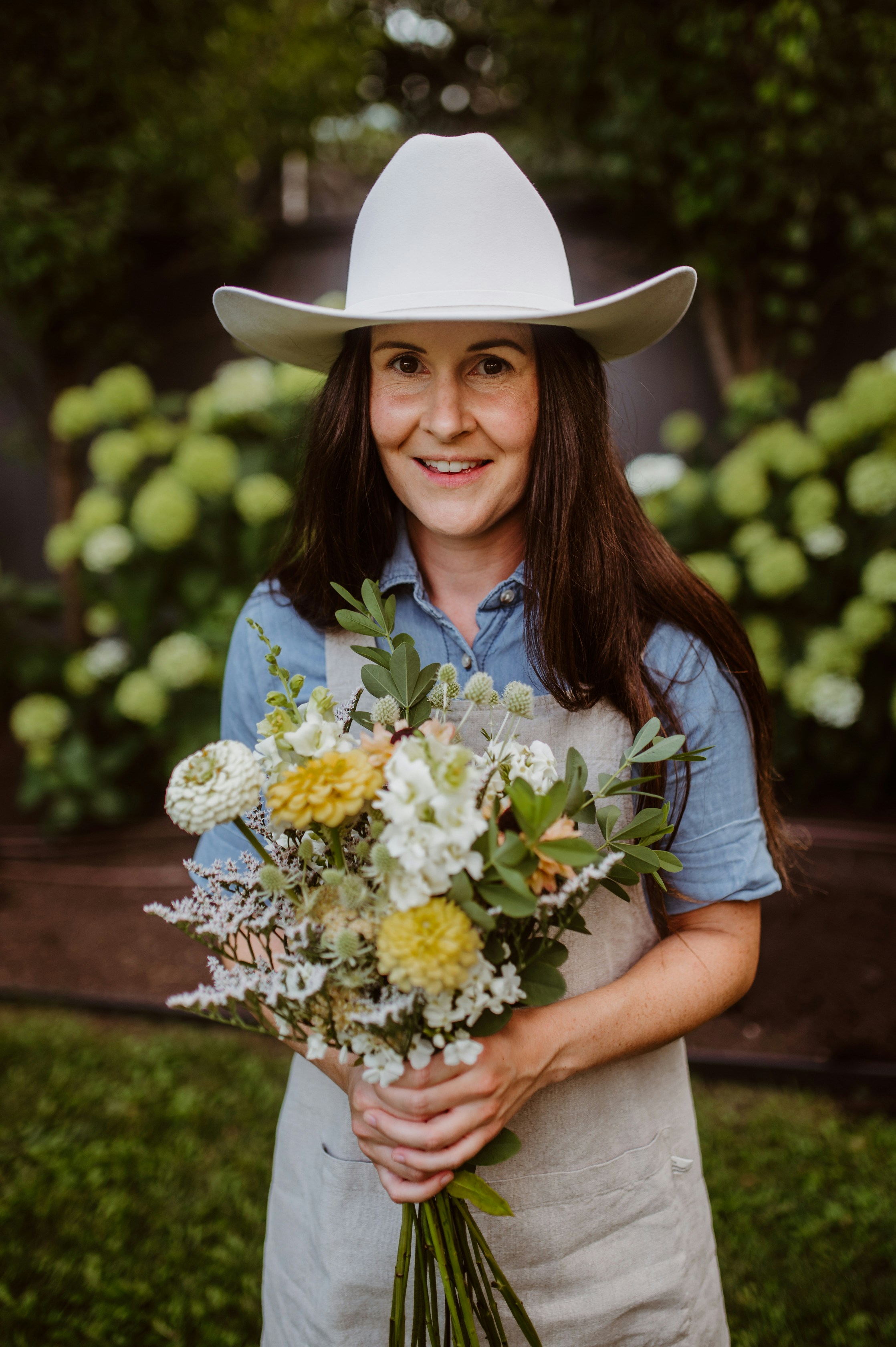 A woman wearing a cowboy hat holding a bouquet of flowers photo – Free ...