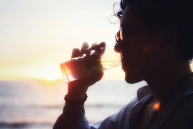 A man drinking from a wine glass in front of the ocean