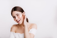 A woman in a white shirt is smiling and touching her face