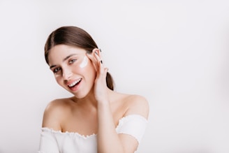 A woman in a white shirt is smiling and touching her face