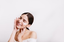 A woman in a white dress smiling and touching her face