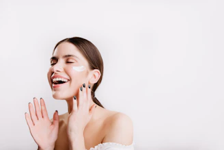 A woman in a white dress smiling and touching her face