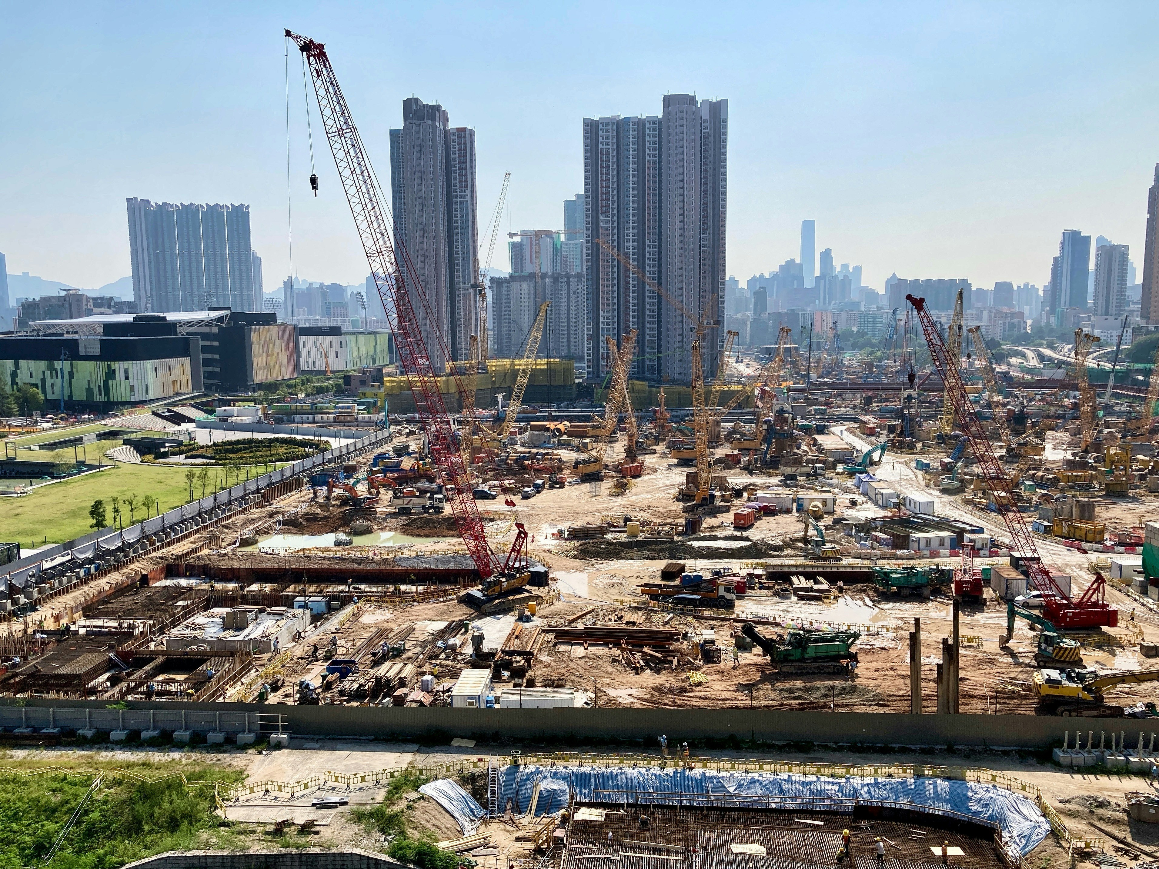 Construction site with buildings under development, workers and heavy equipment, daytime clear sky